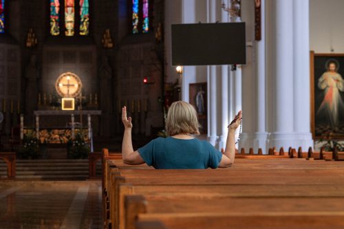 woman sitting in church pew praying with rosary in hand
